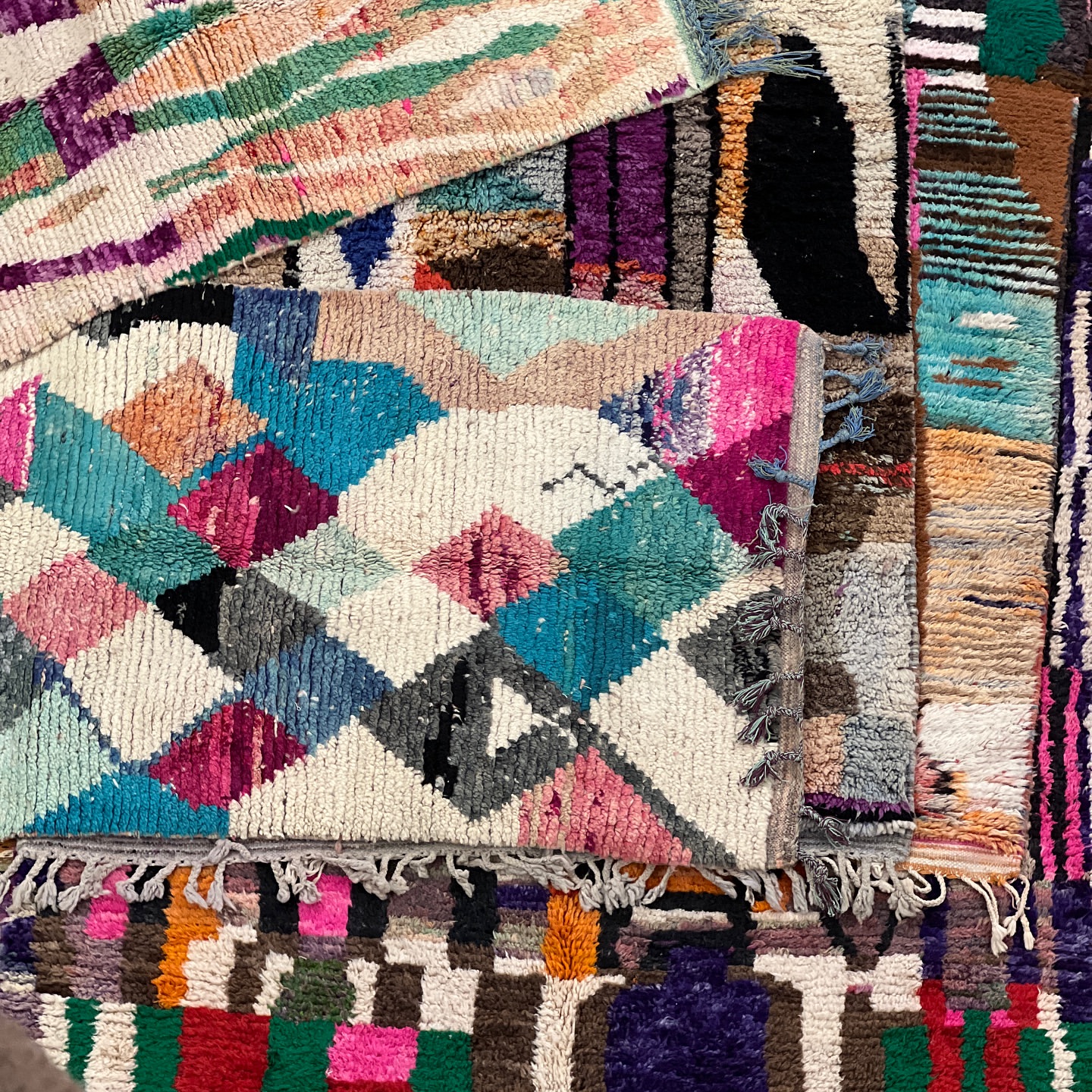 Arrangement of colorful, patterned Moroccan rugs with tassels, featuring diamond and geometric designs. Interior design and textile concepts.