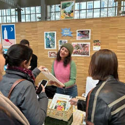 Illustrator Beya Rebaï smiling behind a wooden display table selling art prints to customers