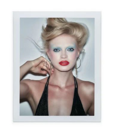 Close-up portrait of a blonde woman with blue eyeshadow, red lipstick, and large hoop earrings wearing a black top.
