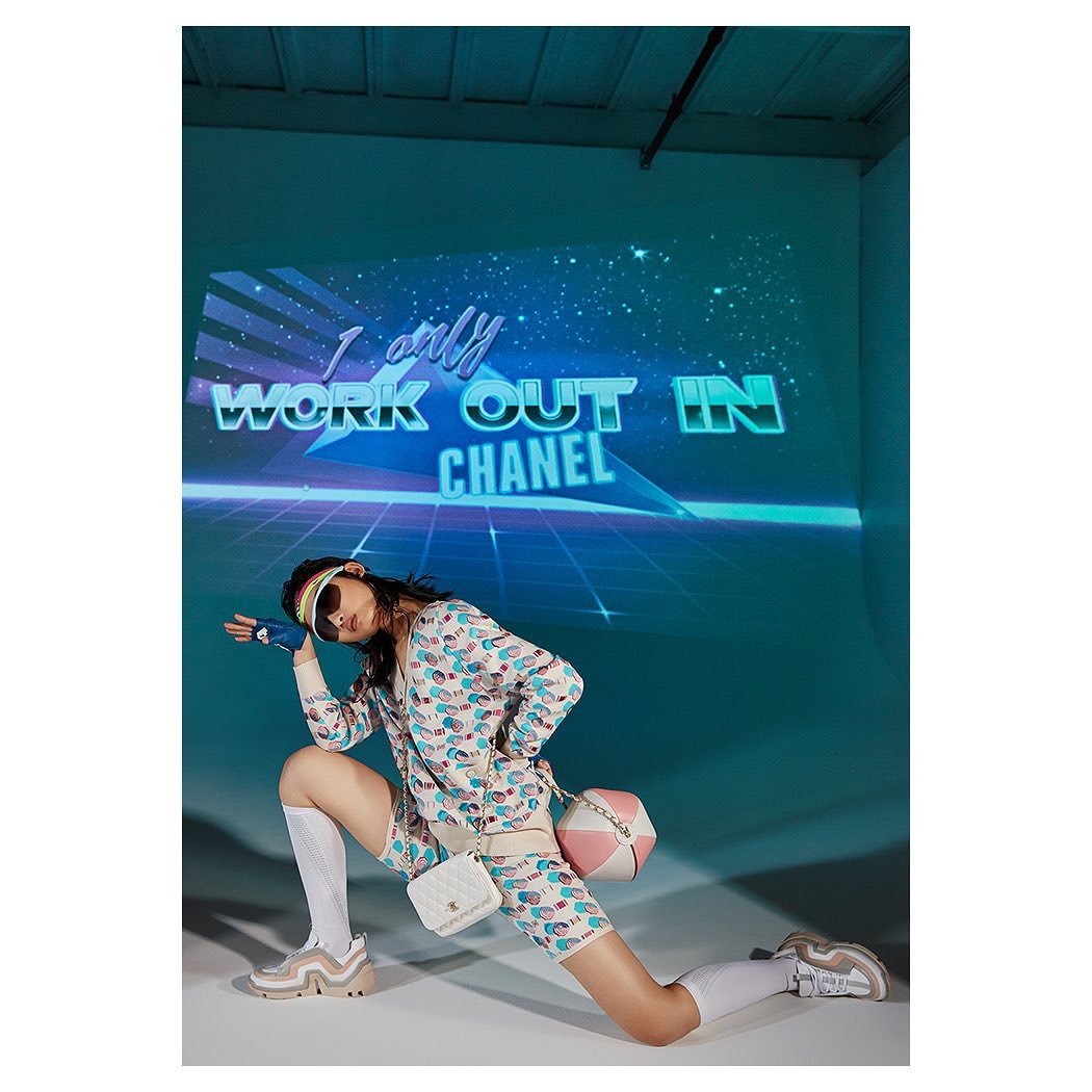 Woman in patterned jacket and bike shorts strikes a pose in a modern studio with a retro graphic projected on the wall behind her.