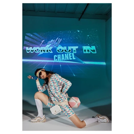 Woman in patterned jacket and bike shorts strikes a pose in a modern studio with a retro graphic projected on the wall behind her.