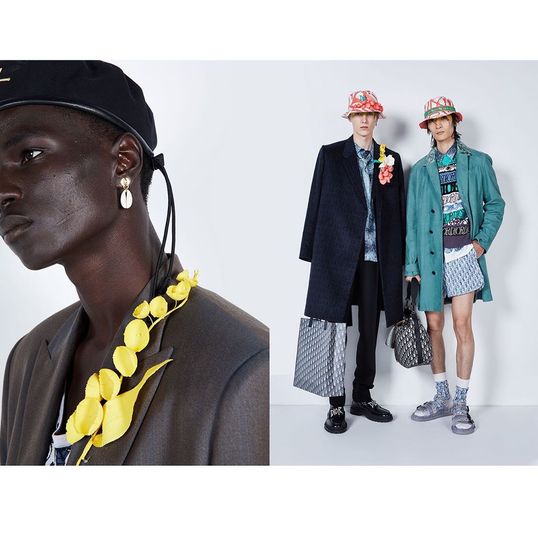 Three male fashion models pose in a photo studio wearing high-fashion clothing, accessories, and statement jewelry against a white backdrop.