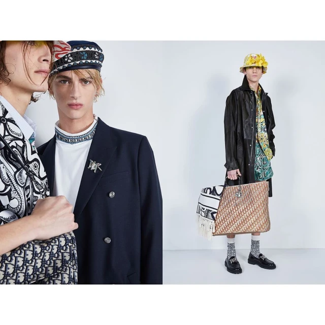 Two young adult fashion models pose in a photo studio wearing designer blazers, bucket hats, and carrying logo printed bags and accessories.