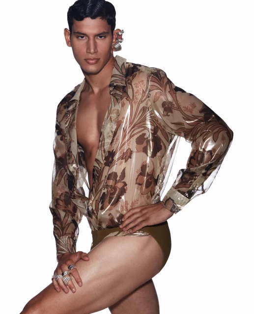 Male model poses in a semi-transparent floral shirt and briefs against a white backdrop, showcasing a fashion-forward and bold style.