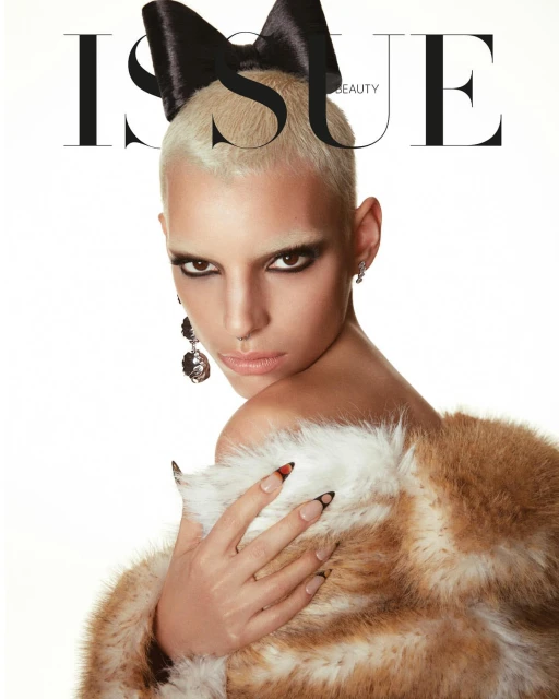 Beauty shot of a woman with a short blonde haircut, dramatic eye makeup, and a large black bow in her hair, wearing a fur shawl.