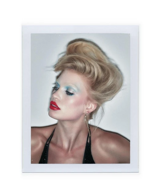 Elegant blonde woman in makeup and black dress posing against a white background, styled in a modern polaroid frame for a fashion shoot.