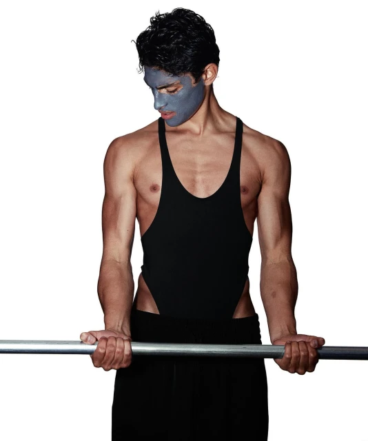 Man with blue facial mask performing bicep curl with barbell in a white background setting, wearing black spandex and black pants.