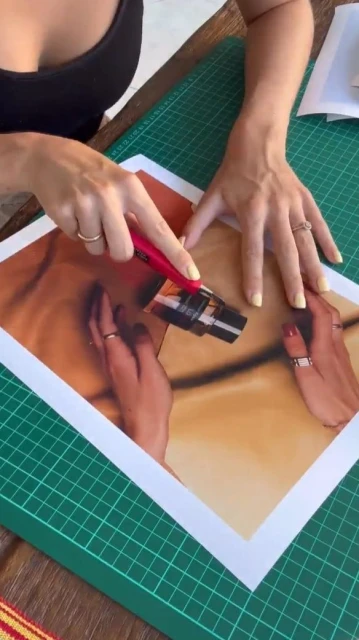Woman's hands craft art, precisely cutting an image on a green cutting mat with a red utility knife under natural light.