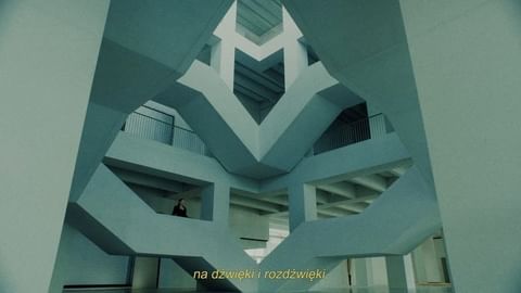 Interior view of a modern architectural structure with geometric patterns, multiple levels, and a lone individual on a higher level.