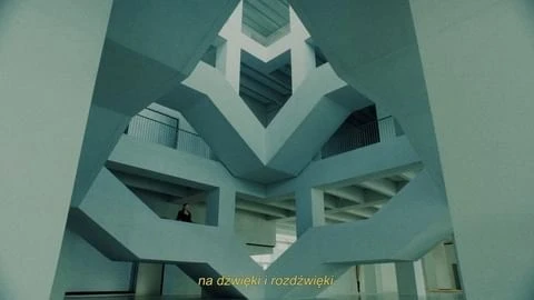 Interior view of a modern architectural structure with geometric patterns, multiple levels, and a lone individual on a higher level.