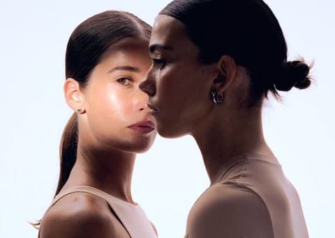 Portrait of two women with dark hair styled in buns against a bright white background, illustrating minimalist beauty