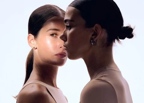 Portrait of two women with dark hair styled in buns against a bright white background, illustrating minimalist beauty