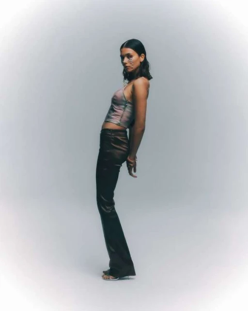 Adult female in brown pants and halter top posing in studio with silver glitter makeup around her eyes in a full shot.