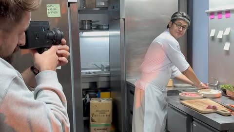 Behind-the-scenes shot of a chef in a commercial kitchen; the videographer is holding a Super 8 camera capturing the culinary scene.