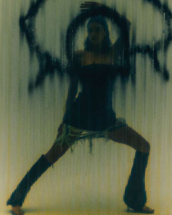 Fashion shot of a woman in an expressive pose with dark clothing and leg coverings, set against a textured background with graphic elements.