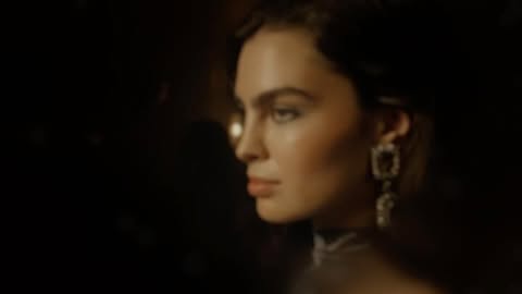 Profile portrait of a woman wearing ornate crystal drop earrings against a dark background.