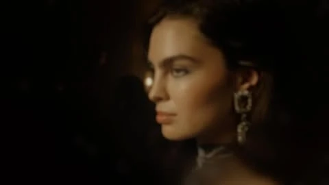 Profile portrait of a woman wearing ornate crystal drop earrings against a dark background.