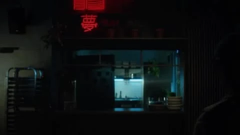 Dark interior shot with neon sign, pass-through to a bright commercial kitchen, and a figure standing near a striped wall.