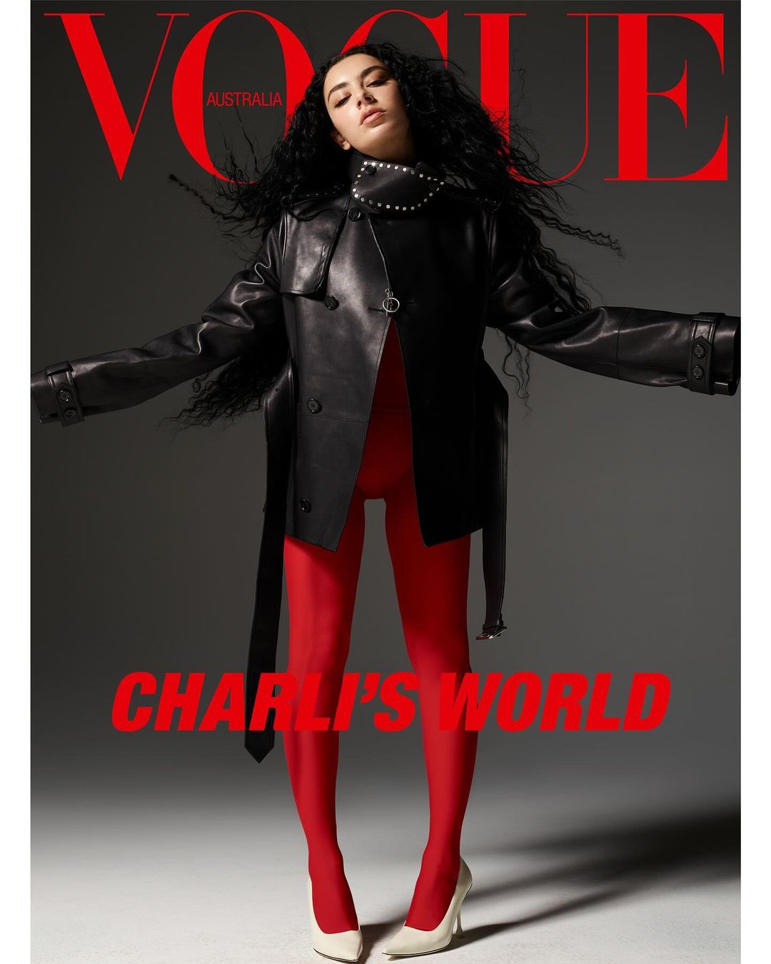 Vogue Australia cover featuring a woman with black curly hair wearing a black leather jacket, red tights, and white heels, set against gray backdrop.