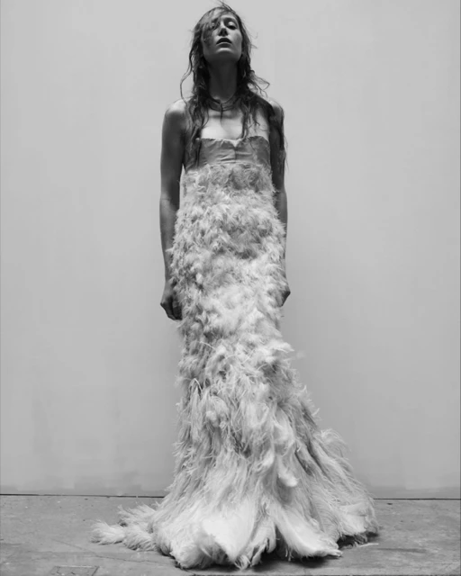 A slender woman with long hair is wearing a feathered gown in this striking black and white studio fashion shot, capturing elegance.