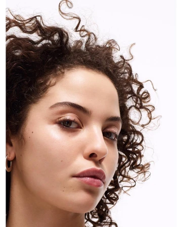 Close-up portrait of a woman with curly brown hair and natural makeup against a plain white background
