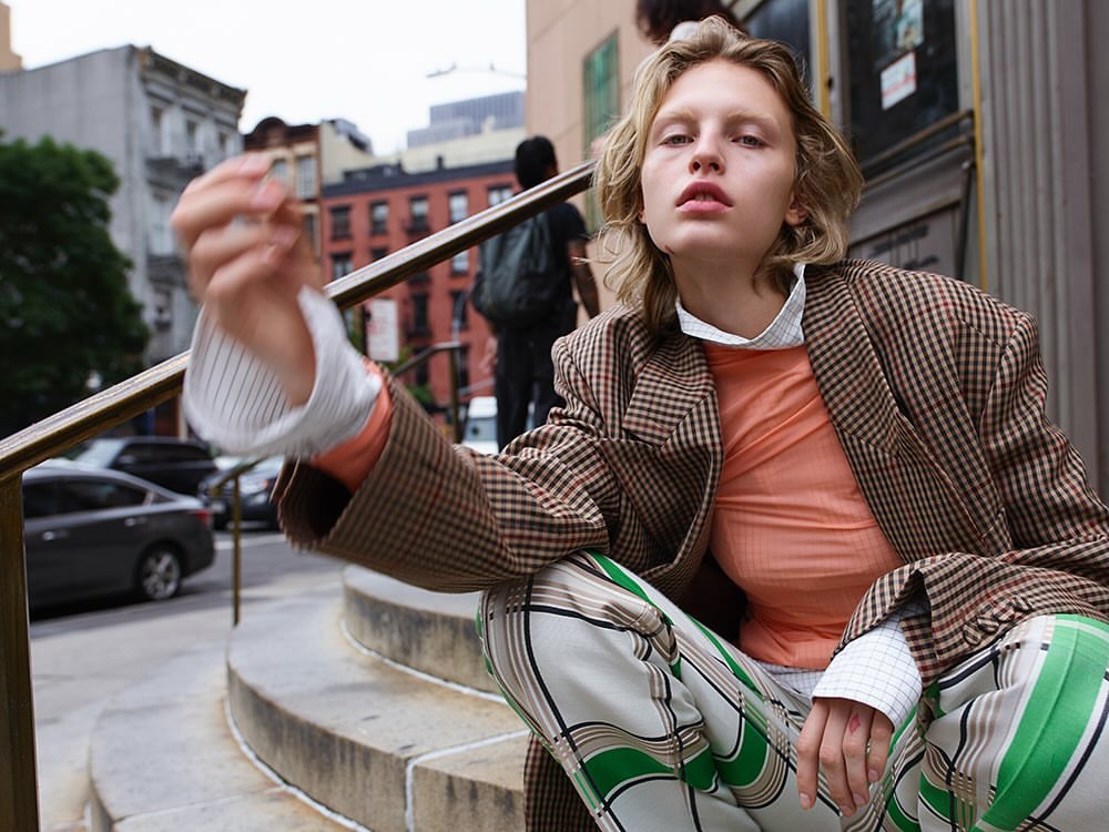 Model in plaid blazer and patterned pants squatting outdoors on stone steps photographed by Amy Troost