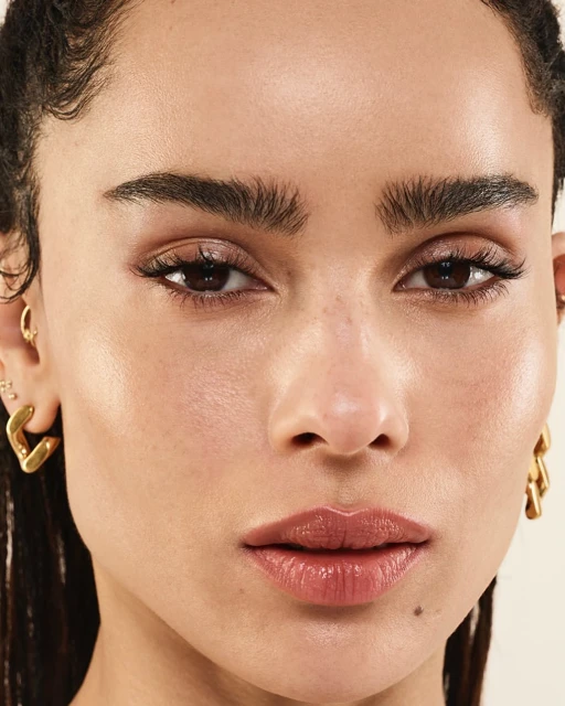 Close-up portrait of a brunette adult female with gold earrings, neutral makeup, and defined eyebrows against a neutral background.