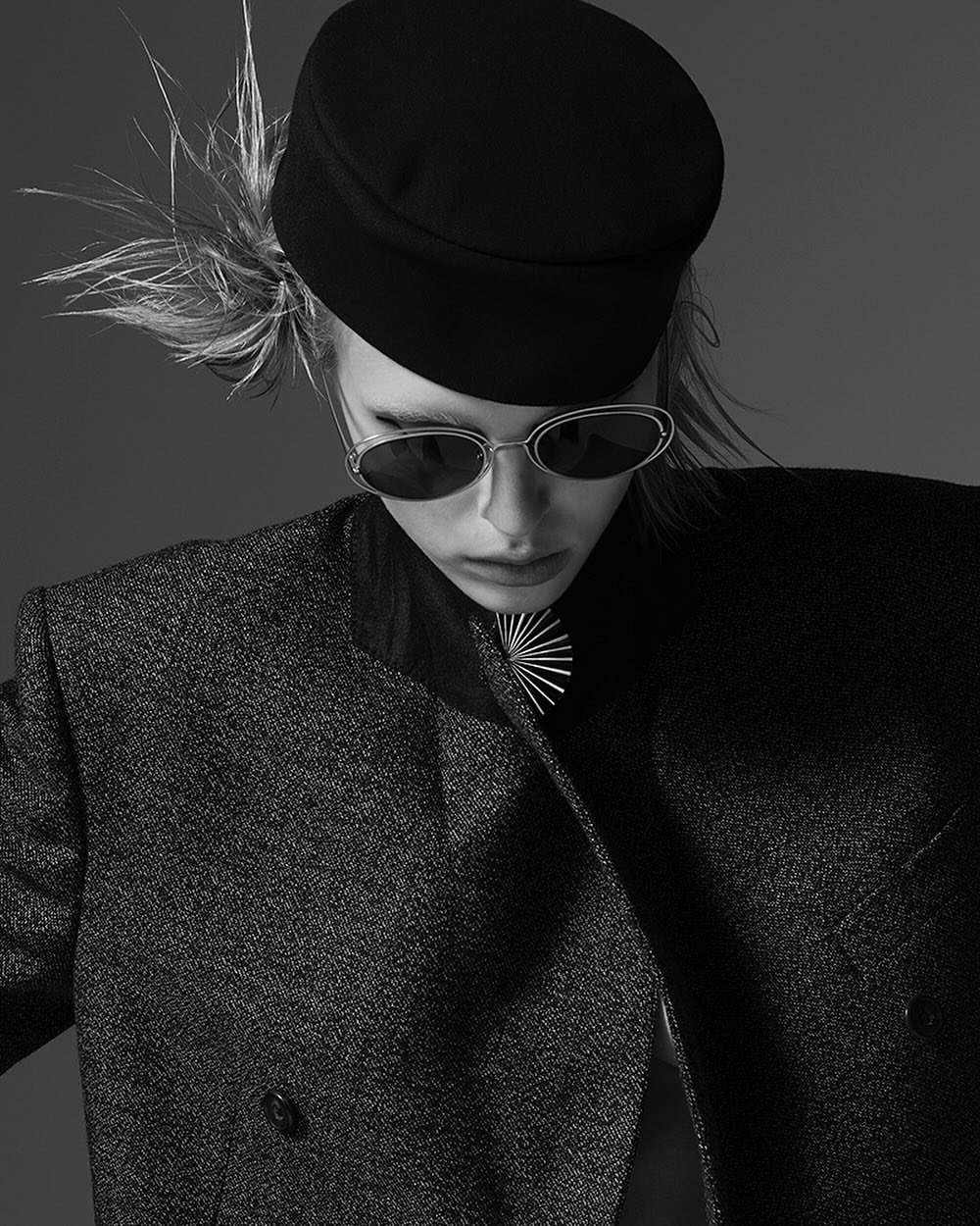 Monochrome portrait of a model wearing a dark flat cap, sunglasses, and structured blazer by Amy Troost.