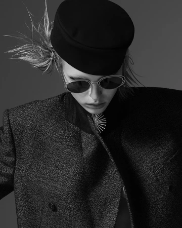 Monochrome portrait of a model wearing a dark flat cap, sunglasses, and structured blazer by Amy Troost.