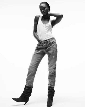 Black and white portrait of a black woman wearing a white tank top and jeans against a white background.