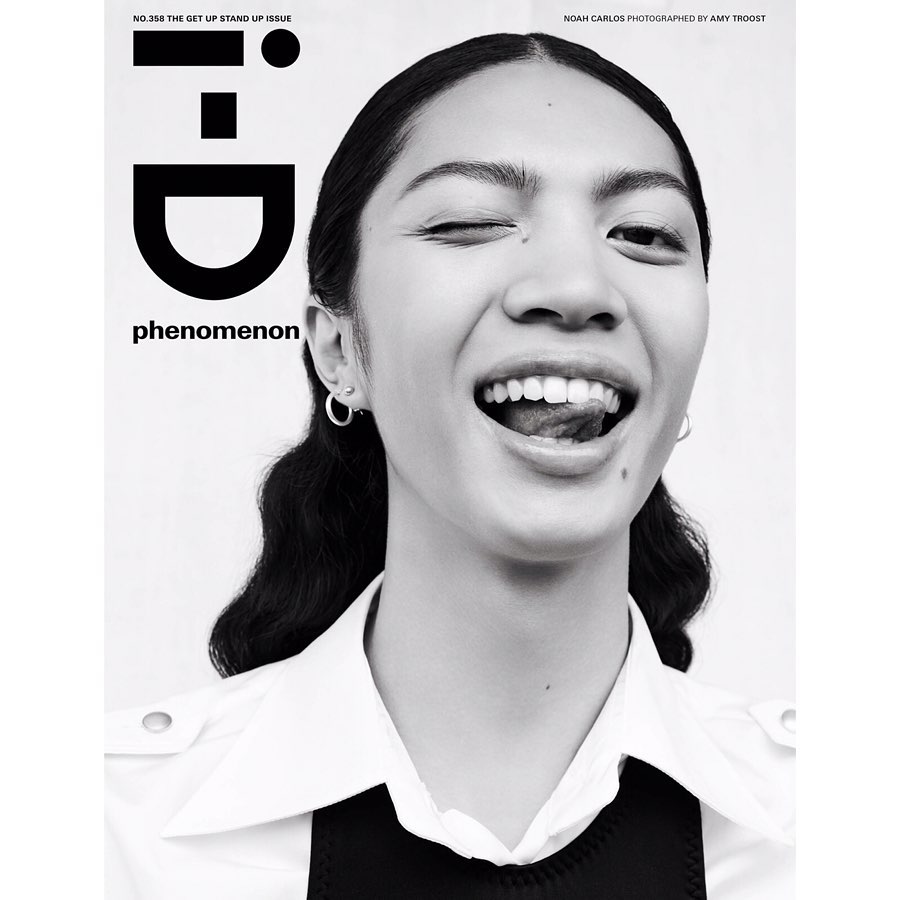 Close-up black and white portrait of a winking woman with her tongue out, wearing a collared shirt, set against a white backdrop.