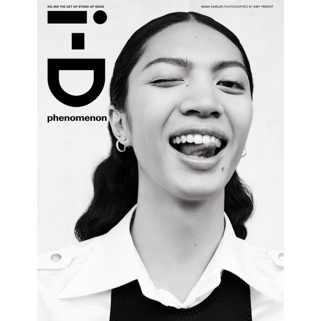 Close-up black and white portrait of a winking woman with her tongue out, wearing a collared shirt, set against a white backdrop.