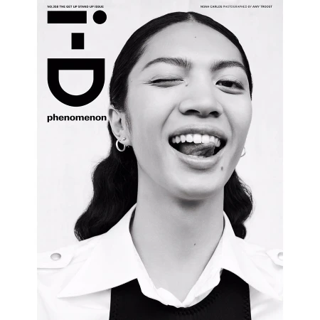 Close-up black and white portrait of a winking woman with her tongue out, wearing a collared shirt, set against a white backdrop.