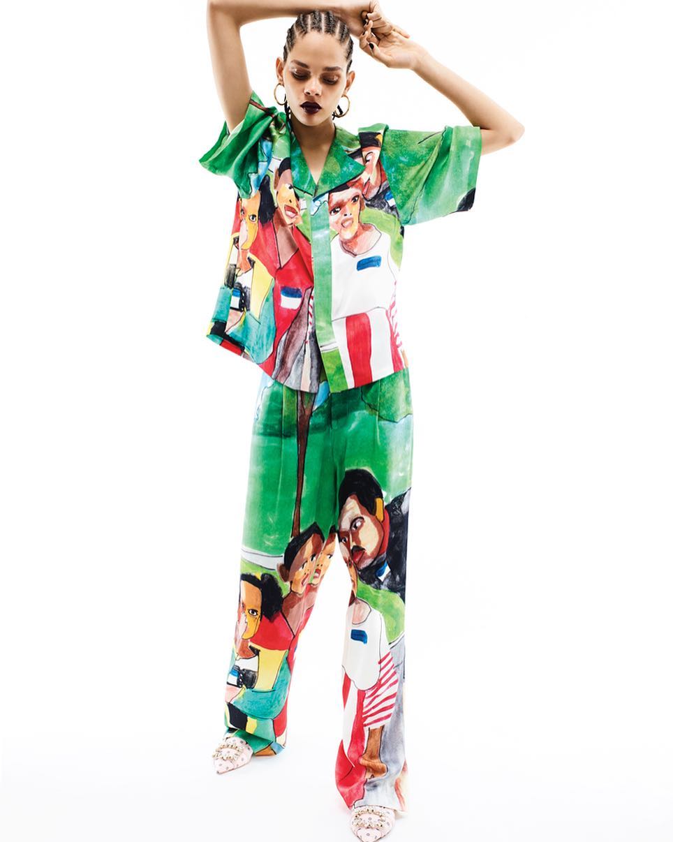 Adult female posing in a patterned, collared shirt and pants against a bright white background in a studio shot for a fashion editorial.