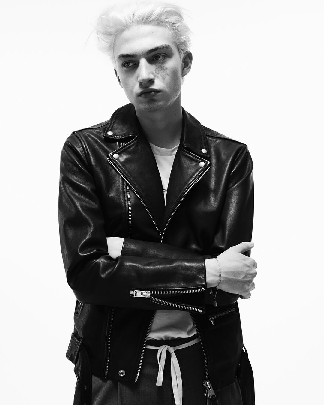 Black and white portrait of a young adult male with platinum hair wearing a leather jacket in front of a white backdrop.