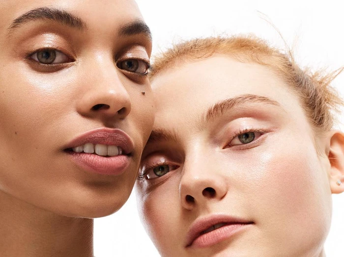 Close-up portrait of two female models with glowing skin and natural makeup against a plain white background