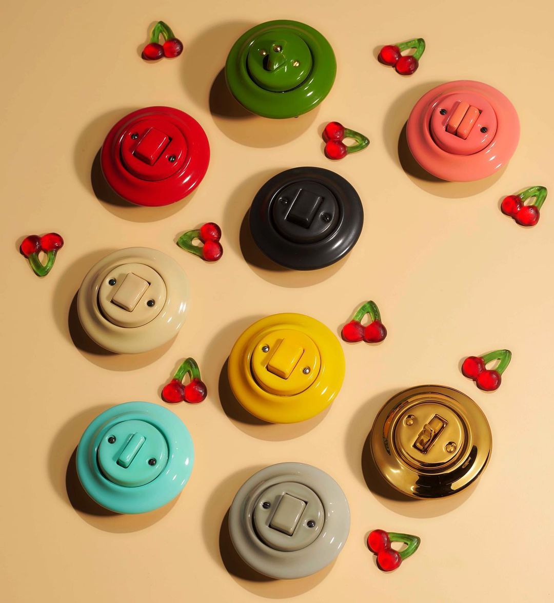 Collection of colorful vintage light switches arranged with cherry candies on a pale peach surface, creating a playful retro aesthetic.