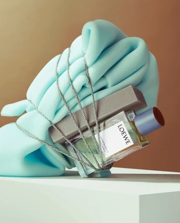 Loewe fragrance bottle wrapped with silver cord and light blue draped fabric on a geometric studio set by Amy Currell