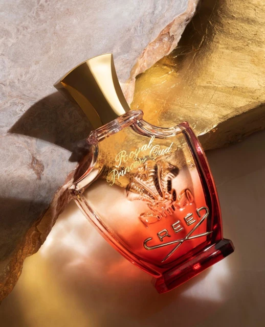 Creed Royal Princess Oud perfume bottle close-up against gold and beige rock textures, highlighting the brand and product details.
