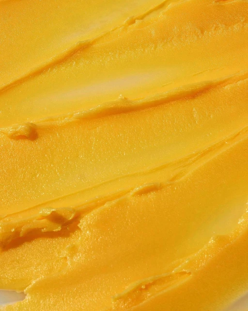 Macro shot of thick, textured yellow cream with ridges, possibly a skincare product, against a white background. Close-up focus.