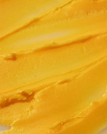 Macro shot of thick, textured yellow cream with ridges, possibly a skincare product, against a white background. Close-up focus.