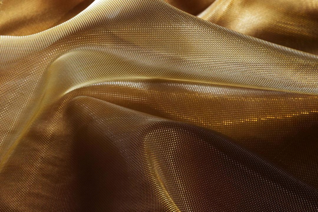 Close-up of gold-colored fabric with a fine, textured weave creating soft, undulating folds and capturing light and shadow.