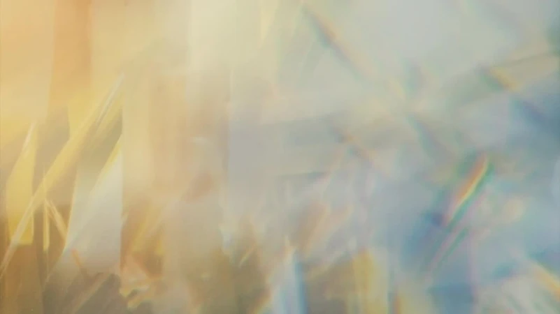 Abstract blurred background of leaves in shades of yellow and blue, with a soft, dreamy aesthetic and subtle rainbow prism.