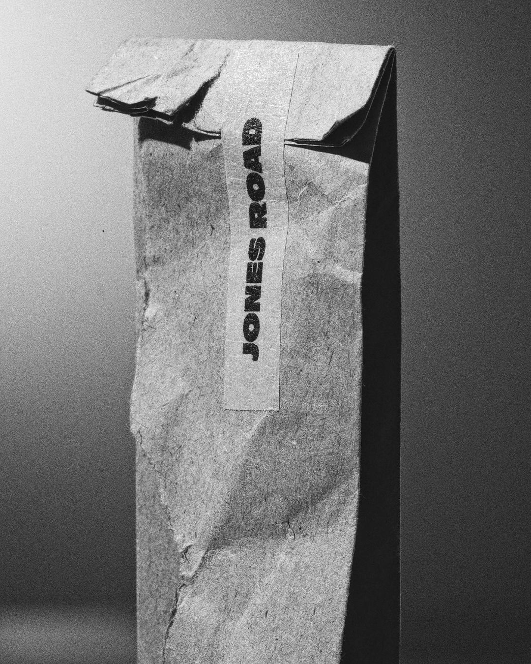 Brown paper bag with 'JONES ROAD' printed vertically on a label, captured in a black and white studio setting with a gradient background.