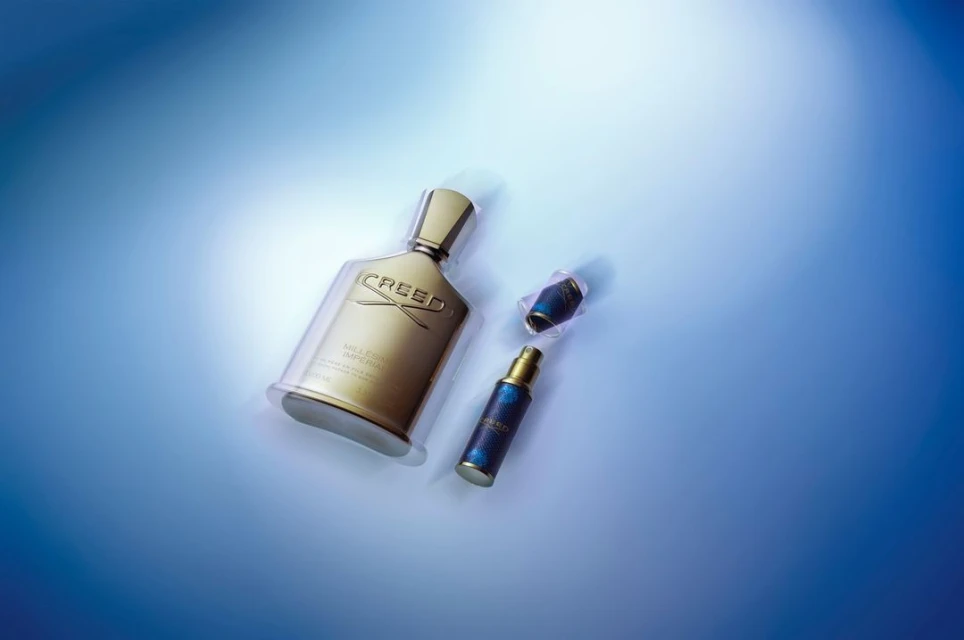 Creed Millesime Imperial fragrance bottle and small travel spray bottle on a blue gradient background. Luxury perfume still life.