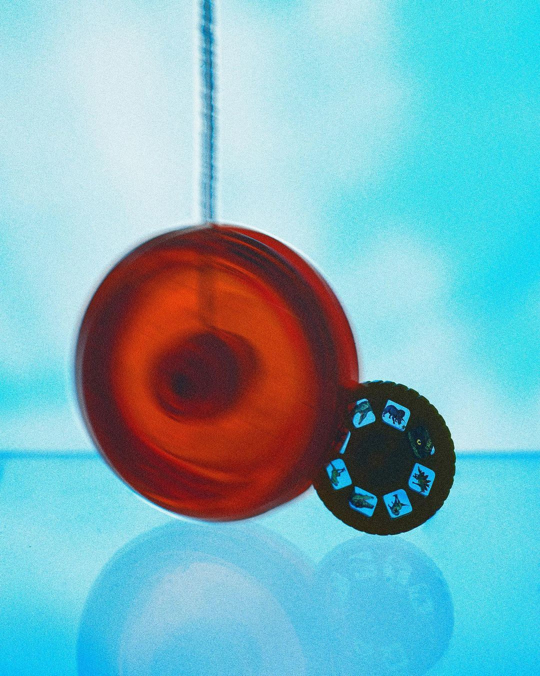 A vibrant still life featuring a red spherical ornament hanging near a vintage stereoscopic viewer, set against a soft blue backdrop.