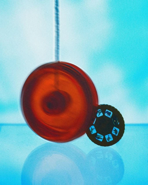 A vibrant still life featuring a red spherical ornament hanging near a vintage stereoscopic viewer, set against a soft blue backdrop.