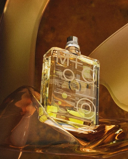 Close-up of a clear glass perfume bottle with metallic accents and geometric designs, set against a warm, textured background.