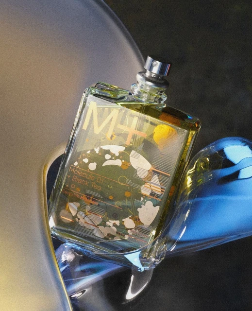 Close-up of a rectangular glass perfume bottle with silver nozzle. The bottle is partially surrounded by abstract shapes.