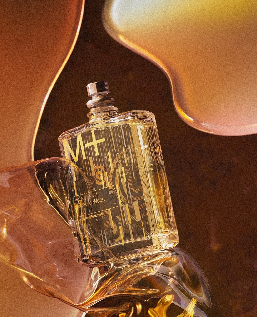 Close-up studio shot of a clear glass perfume bottle with gold accents, surrounded by golden liquid and a blurred golden brown background.